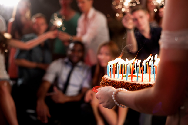 Person carrying birthday cake, group of friends in background